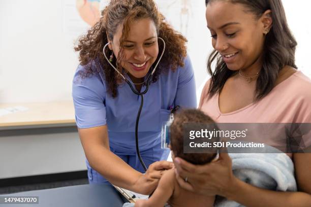 young mom holds baby as doctor listens to his heart - family pediatrician stock pictures, royalty-free photos & images