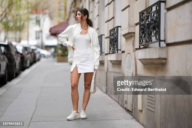 Ketevan Giorgadze wears gold earrings, a gold large chain necklace, a white embossed pattern zipper bomber coat from Les Benjamins, a white tank-top,...