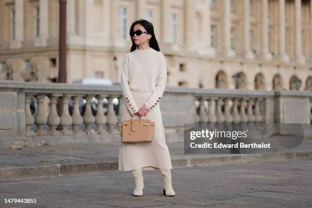 May Berthelot wears black sunglasses from Celine , gold earrings, a white latte ribbed wool with brown buttoned sleeves pullover, a matching ribbed...