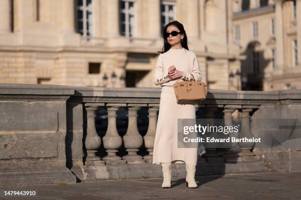 May Berthelot wears black sunglasses from Celine , gold earrings, a white latte ribbed wool with brown buttoned sleeves pullover, a matching ribbed...