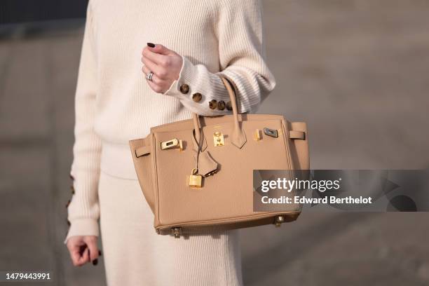 May Berthelot wears a white latte ribbed wool with brown buttoned sleeves pullover, a matching ribbed wool midi skirt, diamonds rings, a gold...