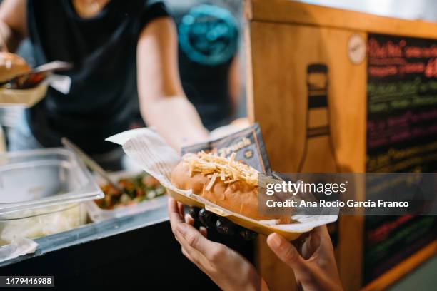 a foodtruck worker woman serving a hot dog to a customer - camion hot dog fotografías e imágenes de stock