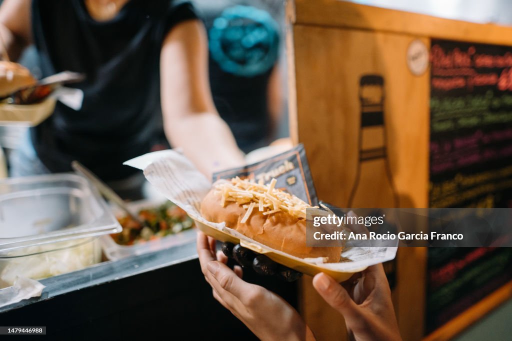 A foodtruck worker woman serving a hot dog to a customer