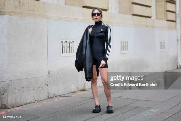 Emy Venturini wears black sunglasses, gold earrings, a black zipper high neck / long sleeves with white striped print pattern logo sleeves / cropped...