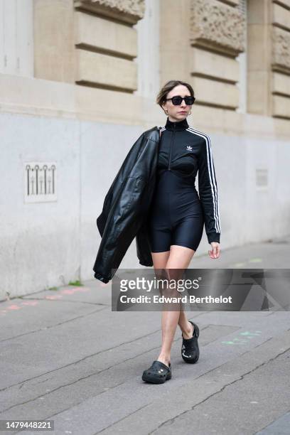 Emy Venturini wears black sunglasses, gold earrings, a black zipper high neck / long sleeves with white striped print pattern logo sleeves / cropped...