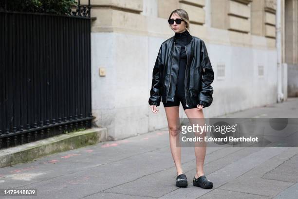 Emy Venturini wears black sunglasses, gold earrings, a black zipper high neck / long sleeves with white striped print pattern logo sleeves / cropped...