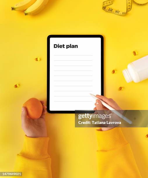 female hand in yellow hoodie writing diet plan in digital tablet. minimalistic healthy dieting flat lay.  well balanced diet, fitness goals setting, lowering cholesterol, nutrition recommendations concept - national diet of japan stock pictures, royalty-free photos & images