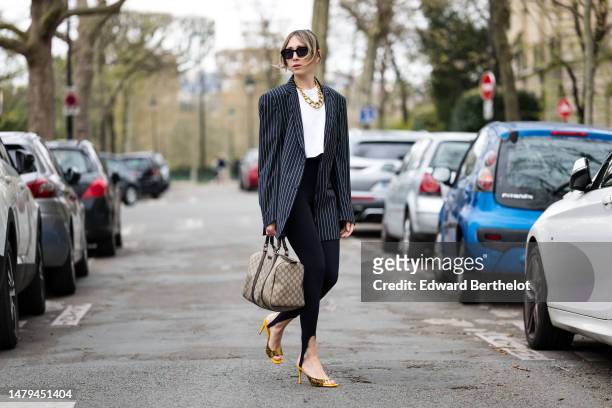Emy Venturini wears black squared sunglasses, gold earrings, a large gold necklace, a white t-shirt, a black with white striped print pattern...