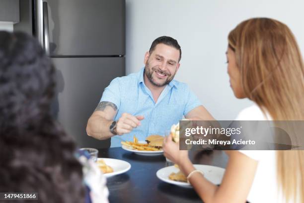 a small group of family members sit together at the table eating food while wearing casual clothing. - mature man smiling 40 44 years blond hair stock pictures, royalty-free photos & images