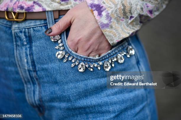 Maria Rosaria Rizzo wears a brown beige shiny leather with gold mini logo buckle belt from Valentino, blue faded denim ripper large pants with...