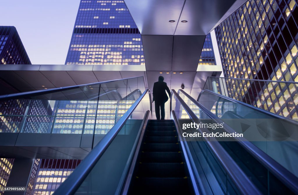 Businessman on top of moving escalator at modern illuminated business district