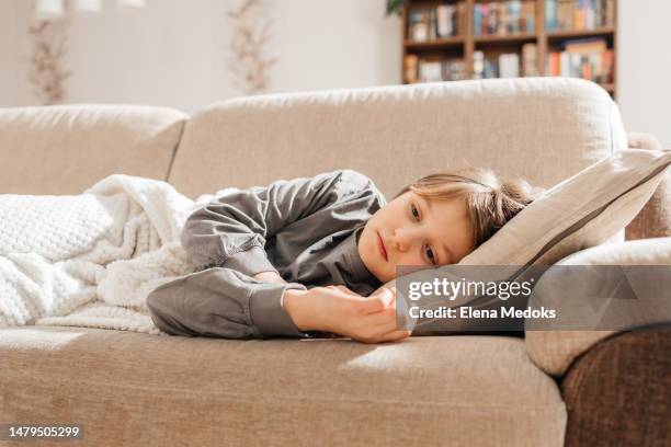 a sick dark-haired teenage girl lies on the couch, covered with a blanket and rests. flu and cold period - disease vector stock pictures, royalty-free photos & images