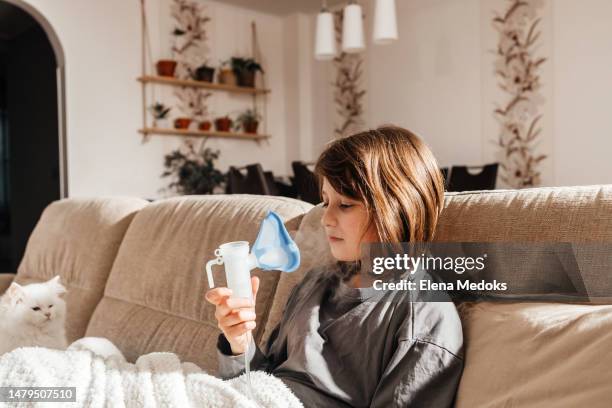 the girl makes an inhalation with a nebulizer while sitting at home in the living room on the couch. treatment at home - respiratory infection stockfoto's en -beelden