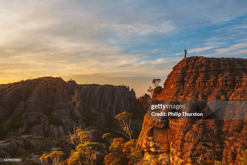 Hiker standing on rock watching sunrise over dramatic mountain landscape
