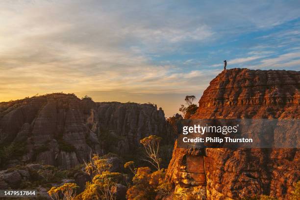 hiker standing on rock watching sunrise over dramatic mountain landscape - top of the mountain australia stock pictures, royalty-free photos & images