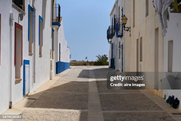 alley with whitewashed houses and cobbled street with access to the sea in the background with a beautiful blue sky - alicante street stock pictures, royalty-free photos & images