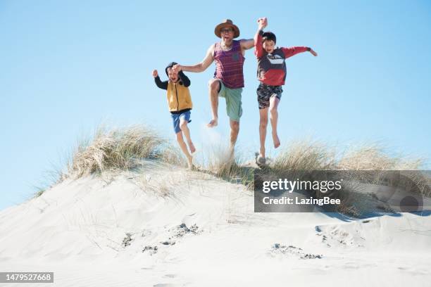 father and children jump in sand dunes - family active lifestyle stock pictures, royalty-free photos & images