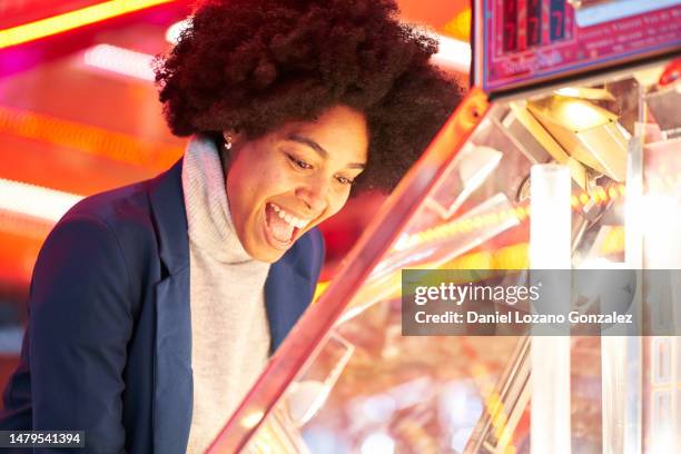 happy woman playing with a claw machine in a fair - mechanical claw stock-fotos und bilder