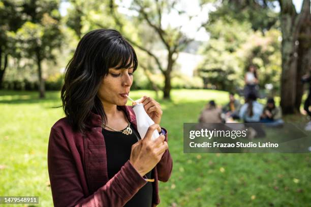 mid adult woman drinking yogurt at public park - lactobacillus stock pictures, royalty-free photos & images