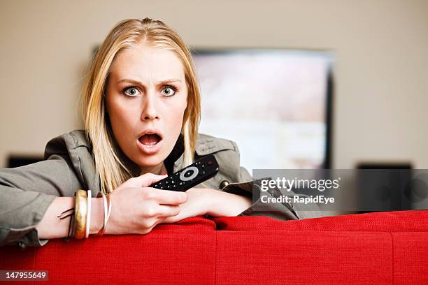 horrified blonde babe holding remote control looks round from television - bad news on tv stock pictures, royalty-free photos & images