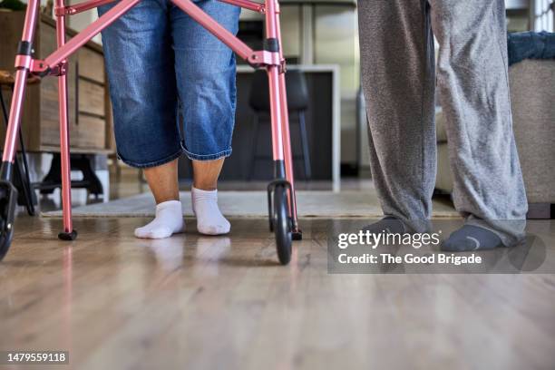 low section of man assisting wife using mobility walker at home - step walker stock-fotos und bilder