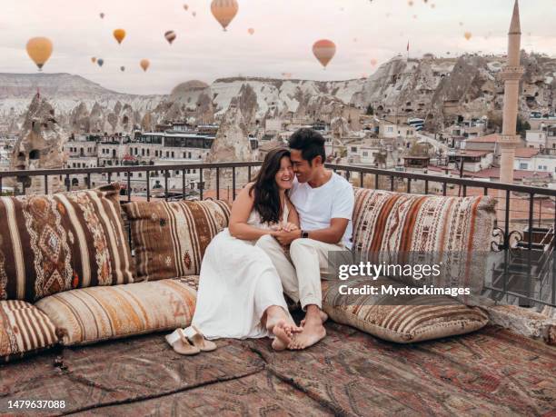 romantic couple in cappadocia sitting on a rooftop and looking at the hot air balloons in the sky - hot filipina women stockfoto's en -beelden