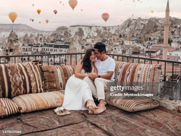 romantic couple in cappadocia sitting on a rooftop and looking at the hot air balloons in the sky - capadócia imagens e fotografias de stock