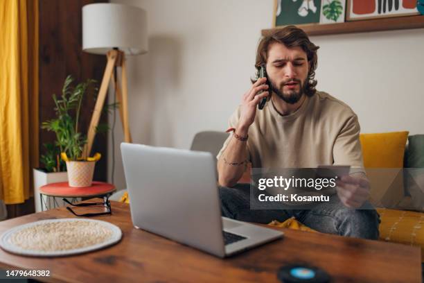 el hombre hace una llamada telefónica mientras intenta hacer una compra en línea con una tarjeta de crédito y una computadora portátil - spoil system fotografías e imágenes de stock