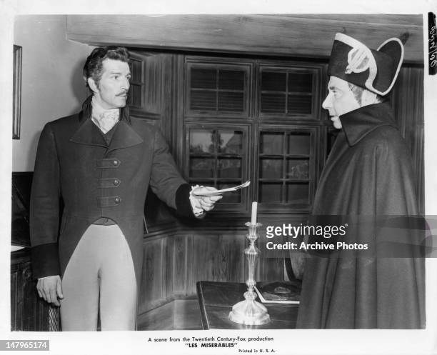 Michael Rennie handing paperwork to Robert Newton in a scene from the film 'Les Miserables', 1952.