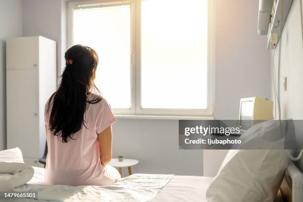 female patient in hospital gown waits for test results - miscarriage stock pictures, royalty-free photos & images