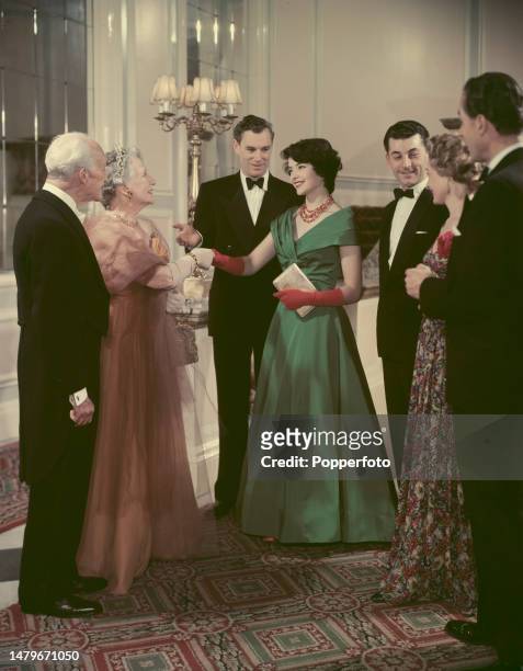 Party scene with a female guest wearing a full length green evening dress being introduced to an older couple at a formal black tie event, London,...