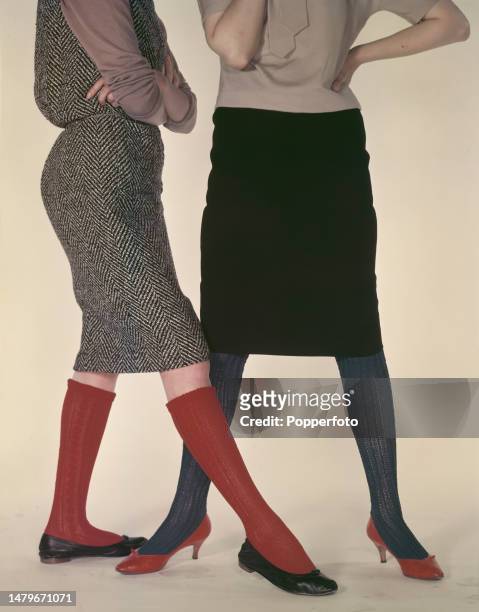 Posed studio portrait of two female fashion models wearing knee length skirts in wool and herringbone tweed and knitted stockings and knee socks in...