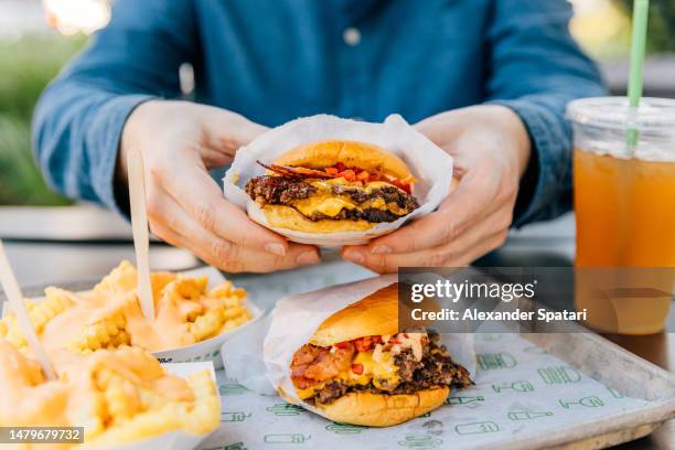 man eating cheeseburger and cheese fries at fast food joint - schnellkost stock-fotos und bilder