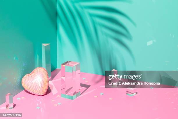 abstract still life 3d scene with composition of crystal glass rectangle blocks prisms,  sparkling heart with sequins, cute kawaii star confetti and tropical palm tree leaf shadow on solid pink and mint green background - mint leaf stock-fotos und bilder