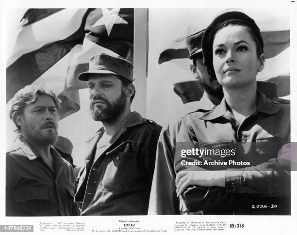 John Vernon and others in uniform stand before Cuban flag in a scene from the film 'Topaz', 1969.