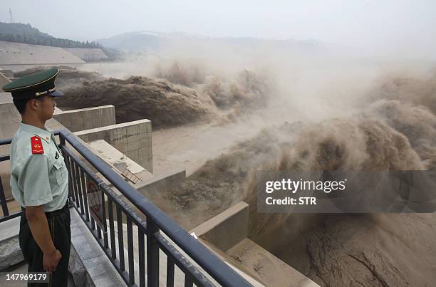 This picture taken on July 6, 2012 shows a Chinese paramilitary guard watching over giant gushes of water being released from the Xiaolangdi dam to...