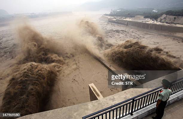 This picture taken on July 6, 2012 shows a Chinese paramilitary guard watching over giant gushes of water being released from the Xiaolangdi dam to...