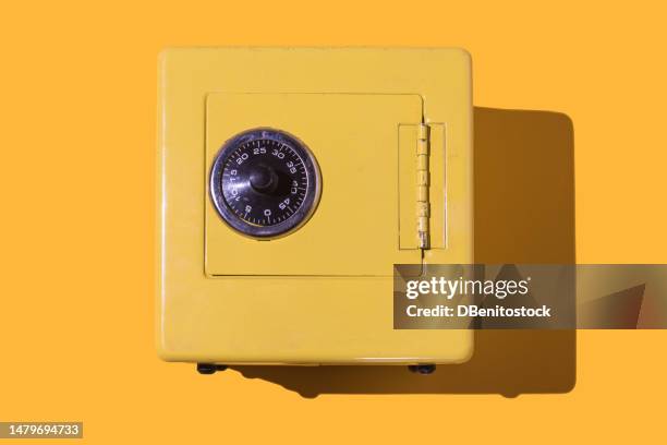 yellow metal safe, with a wheel to insert the key and a letter that reads: 'frontier safe', on a yellow background. saving, treasure, valuable, steal, retro, design and miniature concept. - guarding money stock pictures, royalty-free photos & images