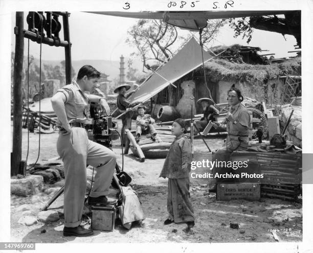 Clark Gable standing next to film equipment as Chinese boy speaks to him in a scene from the film 'Too Hot To Handle', 1938.