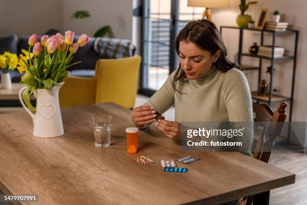young woman sitting at dining table, reading a label on a bottle of prescription medication - blister pack stock pictures, royalty-free photos & images