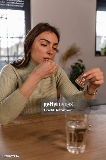 young woman reading a label on a pill packet while taking her medication - blister pack stock pictures, royalty-free photos & images