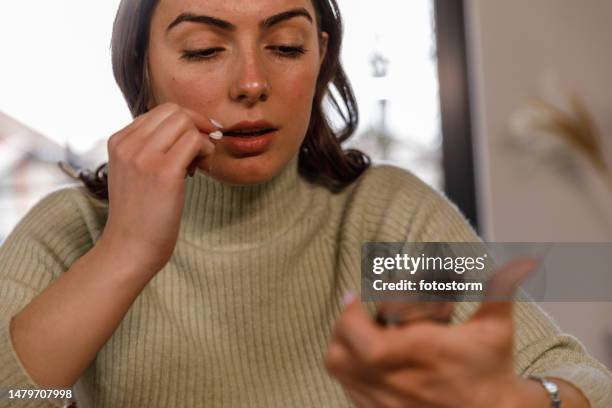 junge frau, die während der einnahme ihrer medikamente ein etikett auf einer pillenpackung liest - antibabypille stock-fotos und bilder