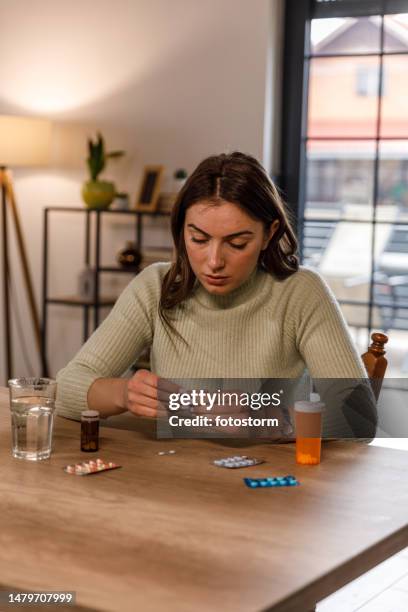 young woman sitting at dining table, preparing to take her prescription medication - blister pack stock pictures, royalty-free photos & images