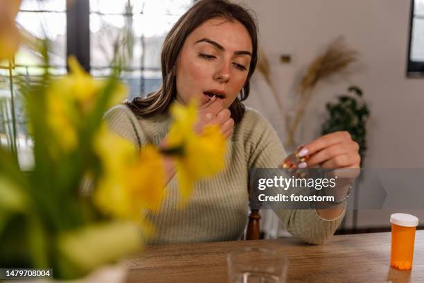 young woman reading a label on a pill packet while taking her medication - blister pack stock pictures, royalty-free photos & images