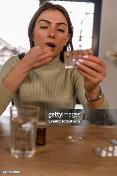 young woman reading a label on a pill packet while taking her medication - blister pack stock pictures, royalty-free photos & images