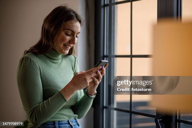 young woman smiling while responding to a text message via smart phone - meme text stock pictures, royalty-free photos & images