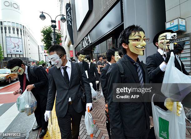 People wearing masks pick up litter as they attend a clean up mission organised by hacker collective Anonymous on a street in Tokyo on July 7, 2012....