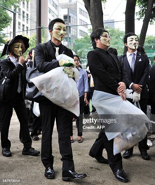 People wearing masks pick up litter as they attend a clean up mission organised by hacker collective Anonymous on a street in Tokyo on July 7, 2012....