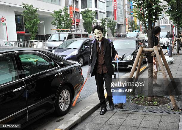 Person wearing a mask sweeps up litter as part of a clean up mission organised by hacker collective Anonymous on a street in Tokyo on July 7, 2012....