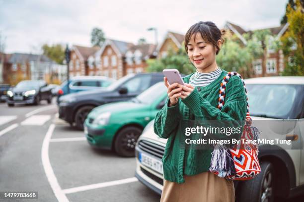 young asian woman making payment for parking place on mobile app with smartphone in car park - happiness meter stock pictures, royalty-free photos & images